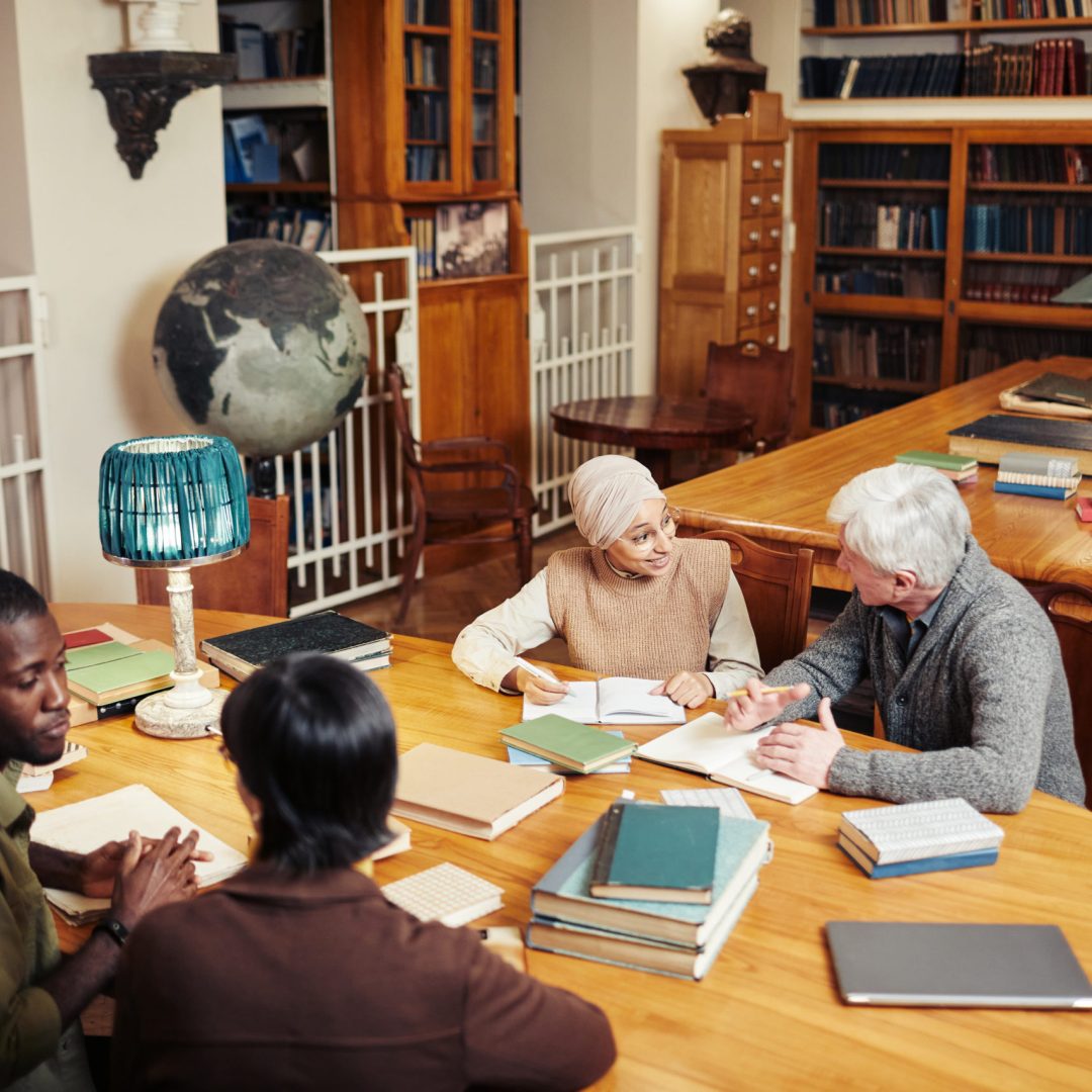 High angle portrait of diverse group of people studying at round table in classic college library, copy space